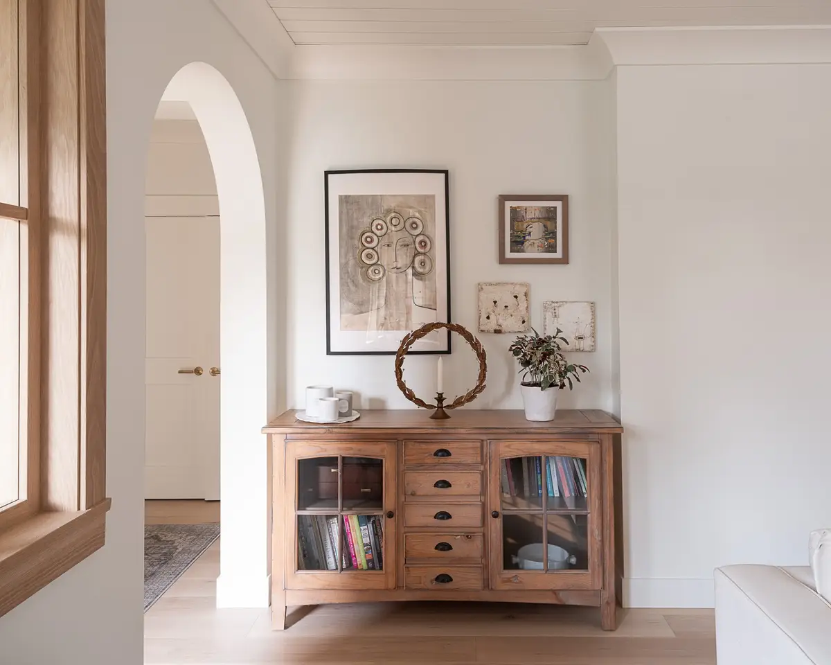 Wood sideboard with glazed doors below framed art, an arched opening to a hall at left