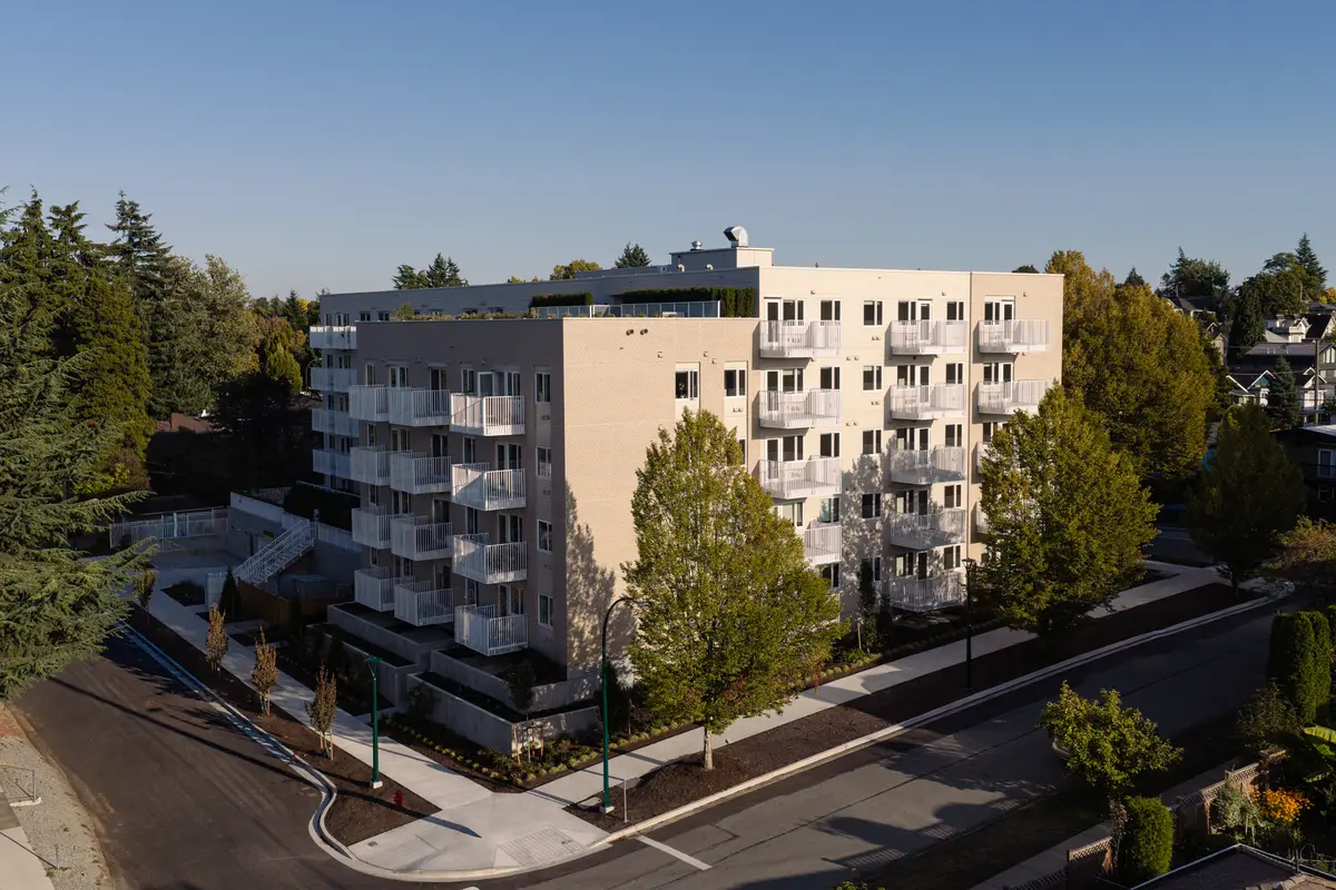 The building on its corner, balconies, street trees and mountains