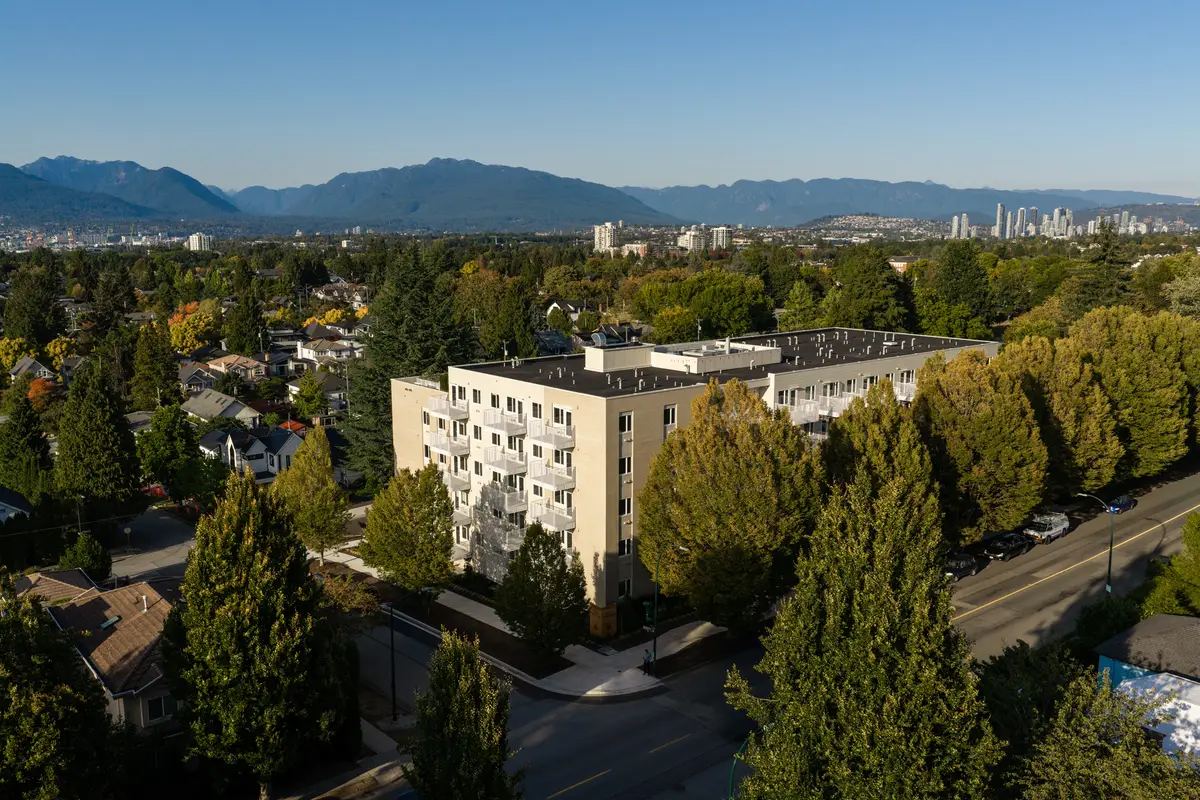 The building from above, set among mature trees with the mountains behind