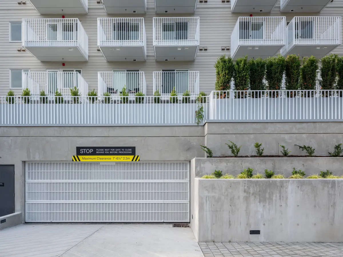 A white garage door, a planted bed, and a balcony with small trees above