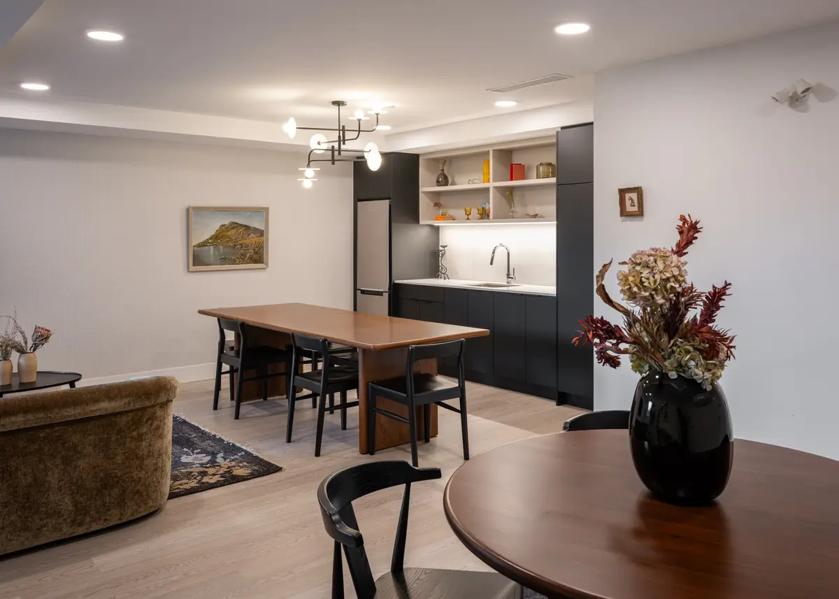 A furnished suite, dining table, sofa, and kitchen beyond