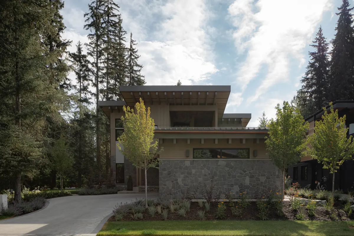 Spring arrival, vertical wood over a stone base, a deep wood soffit, and young trees along the drive