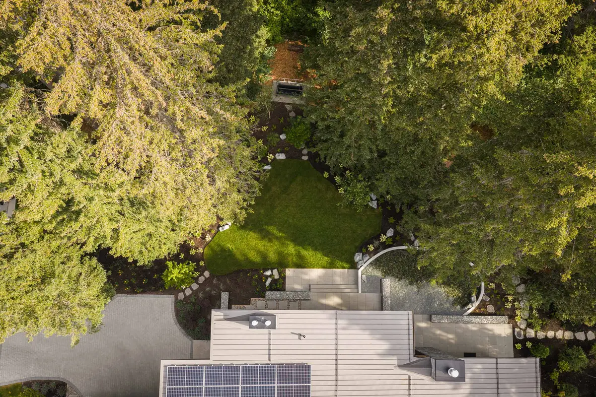 Looking down on the metal roof and a solar array, the curved pool, and a lawn set into the firs