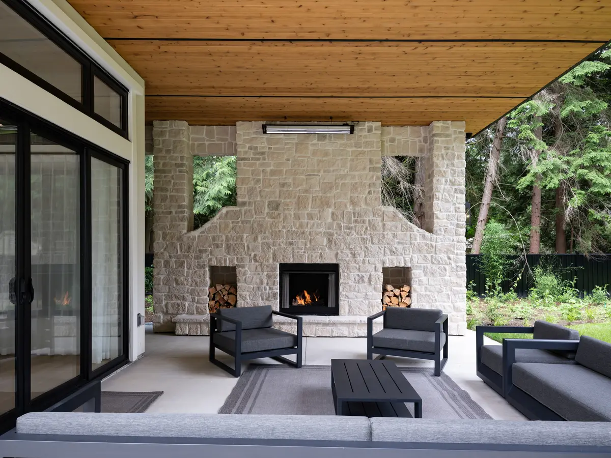 A covered patio with a stone fireplace, sofas, and the forest beyond