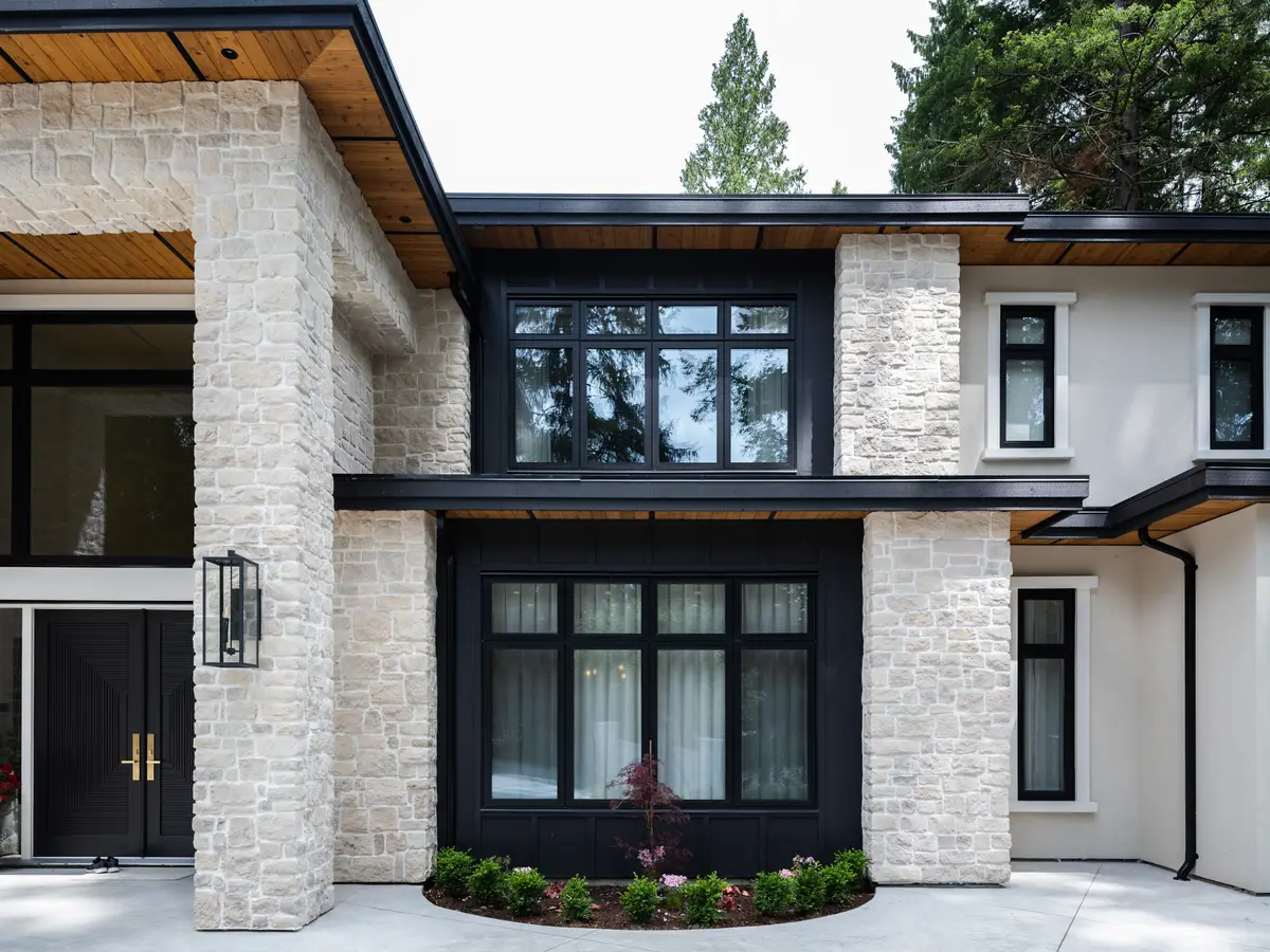 A stone corner of the house, black windows and a planted bed