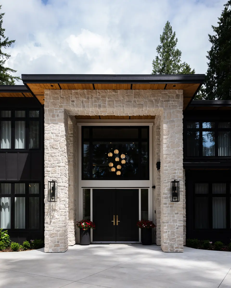 The entry, stone piers and a black door under a wood-lined canopy