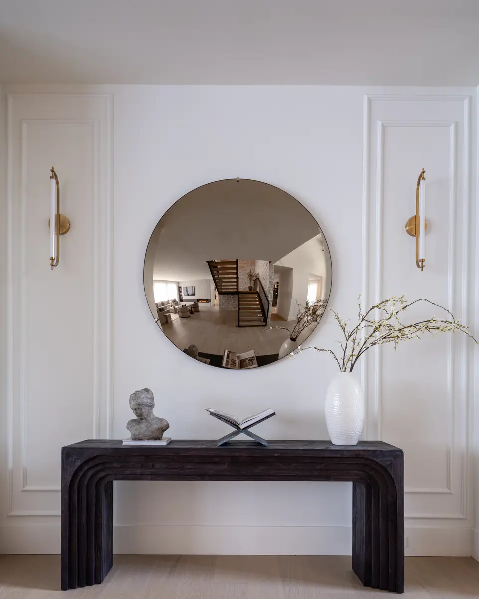 A round mirror over a console in a panelled hall
