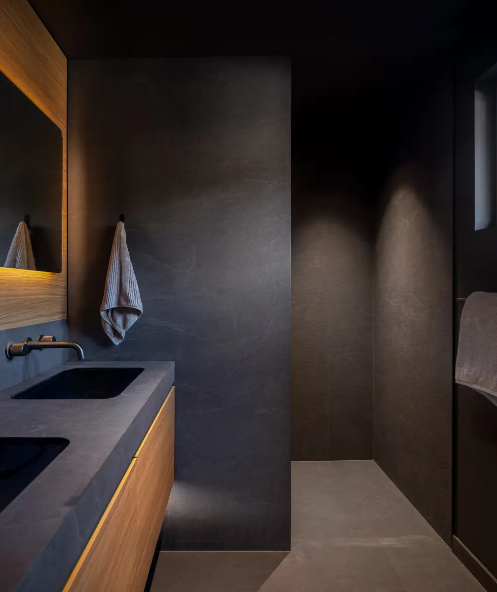 Dark stone bathroom with a wood vanity, two sinks, and a lit mirror at Riverrun Place, Whistler
