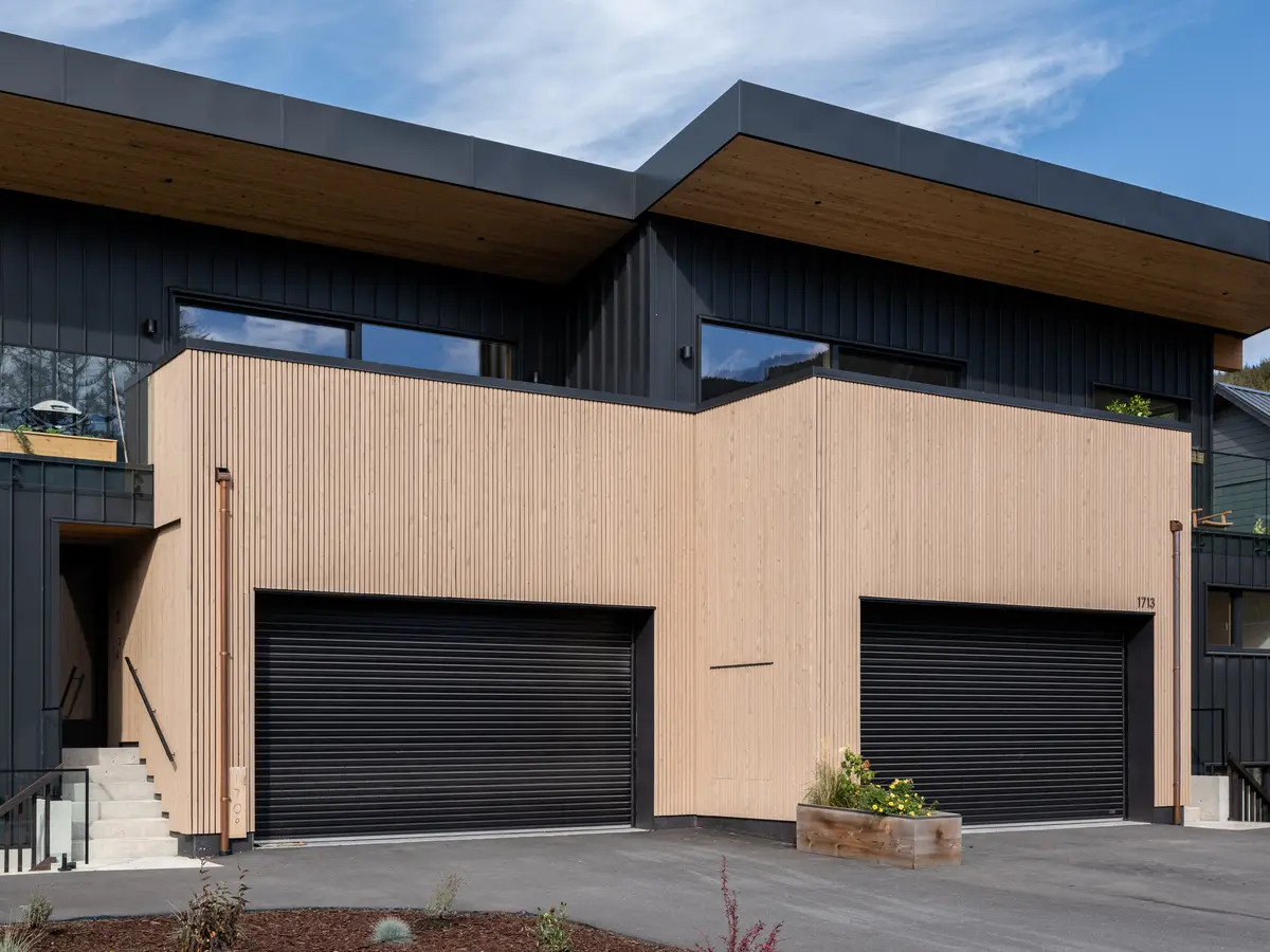 Garage elevation at Riverrun Place, Whistler, vertical wood, black roll-up doors, and a wood soffit