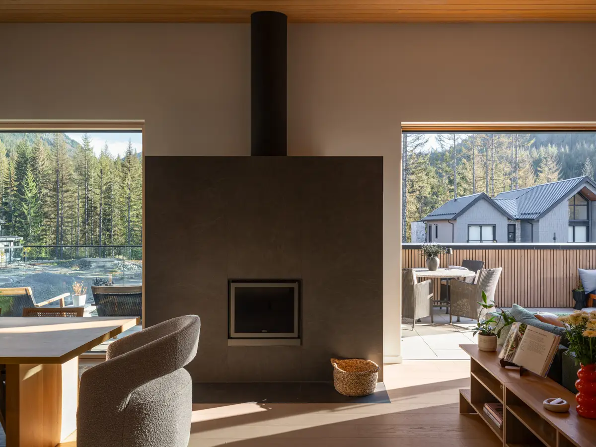 Living room at Riverrun Place, Whistler, a dark stone fireplace between windows to the forest and the deck