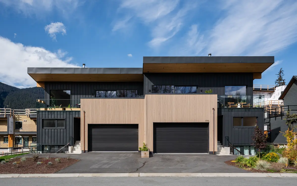 Street elevation of the duplex at Riverrun Place, Whistler, vertical wood and black metal with mountains behind