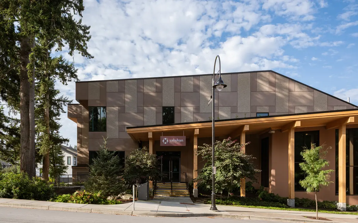 The entry facade seen through evergreens, timber columns under the roof