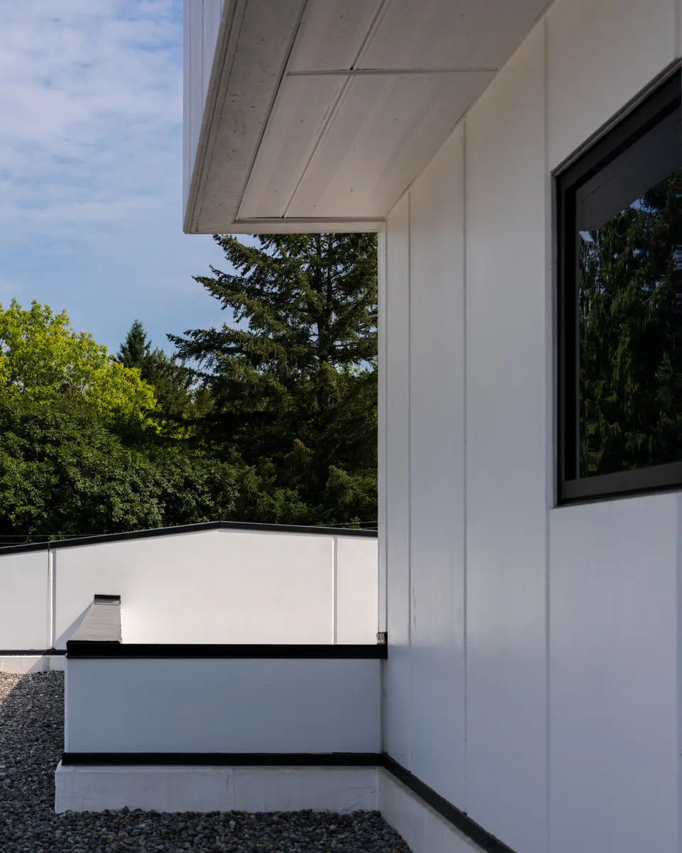 The upper facade, a dark window in a white panel, trees below