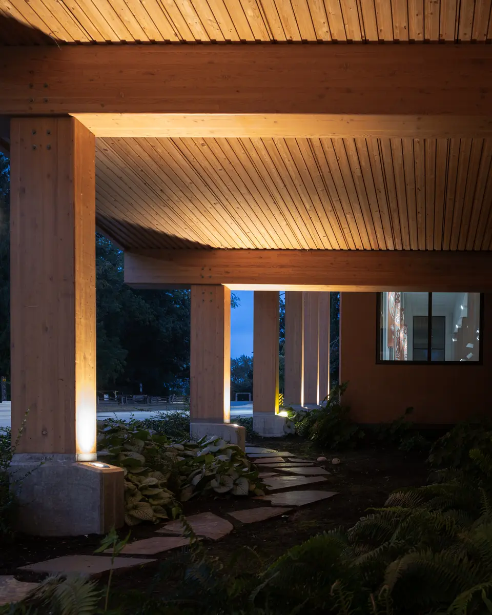 Timber columns and the soffit lit from below at dusk