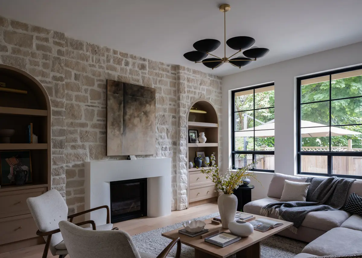 The living room, a stone fireplace and sofas by black-framed windows
