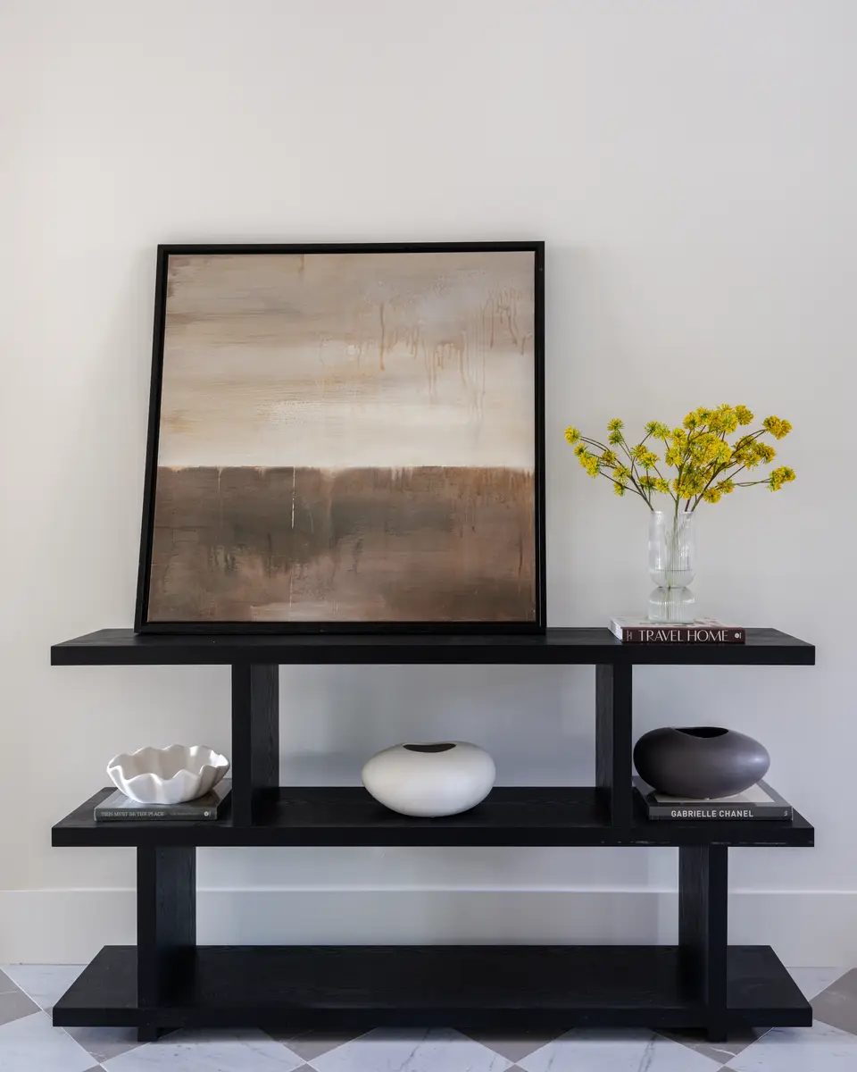 A dark console with a painting and a vase of yellow flowers